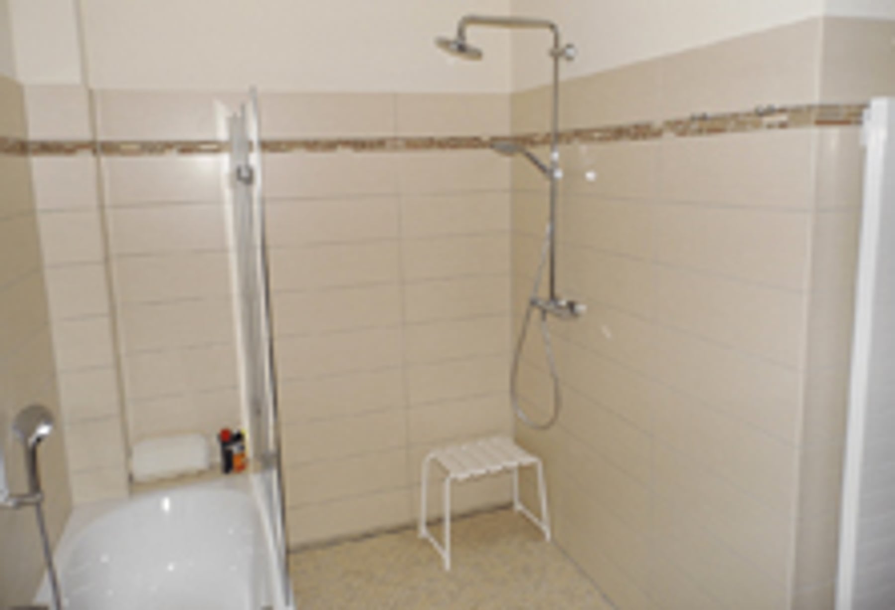 Dusche mit beigen Fliesen und Sitzhocker